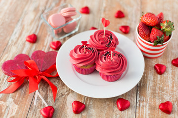 valentines day, sweets and romantic concept - close up of frosted cupcakes, red heart shaped chocolate candies, lollipops and strawberries