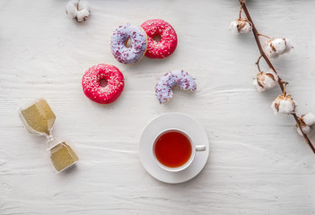 Tasty doughnuts with cup of tea on white wooden table