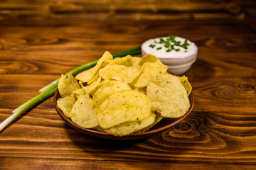 Ceramic plate with potato chips and glass bowl with sour cream on wooden table