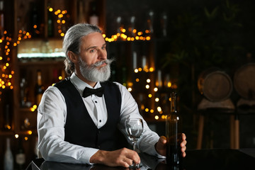 Senior barman with glass and bottle of wine in pub