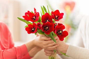 romantic date, valentines day and couple concept - close up of man giving red tulip flowers to woman
