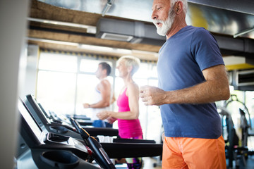 Fototapeta na wymiar Happy senior people running together on treadmills in gym.