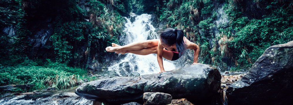 Young woman practice yoga near waterfall in forest