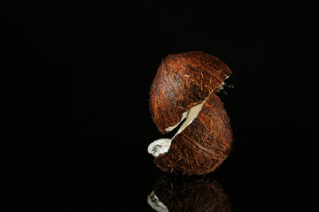 Halves of ripe coconut and splash of water on dark background