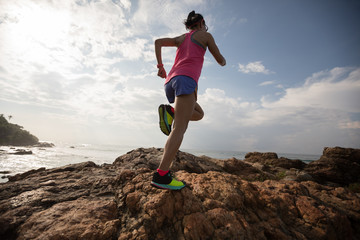 Young fitness woman trail runner running to rocky mountain top on seaside