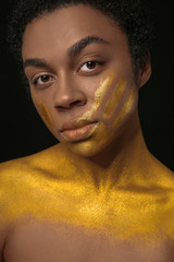 African-American woman with golden paint on her body against black background