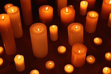 Many burning candles on table in darkness