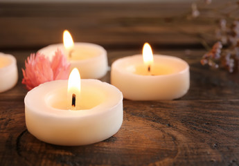 Fototapeta na wymiar Burning candles and flower on wooden table, closeup