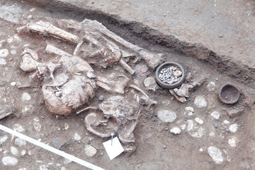 Archaeological excavations. Human remains (bones, skeleton and skull) in the ground, with little found artefacts in the tomb. Real digger process. Outdoors, copy space, close up.