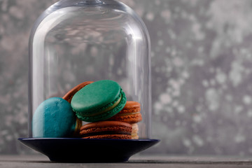 Multi-colored macarons under the glass dome on a gray background. Delicate macarons macaroons