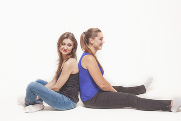 Fototapeta na wymiar Two young caucasian women with dark hair sit back-to-back on the floor, holding their knees, wearing casual (blue and black). Studio, isolated, white background, copy space.
