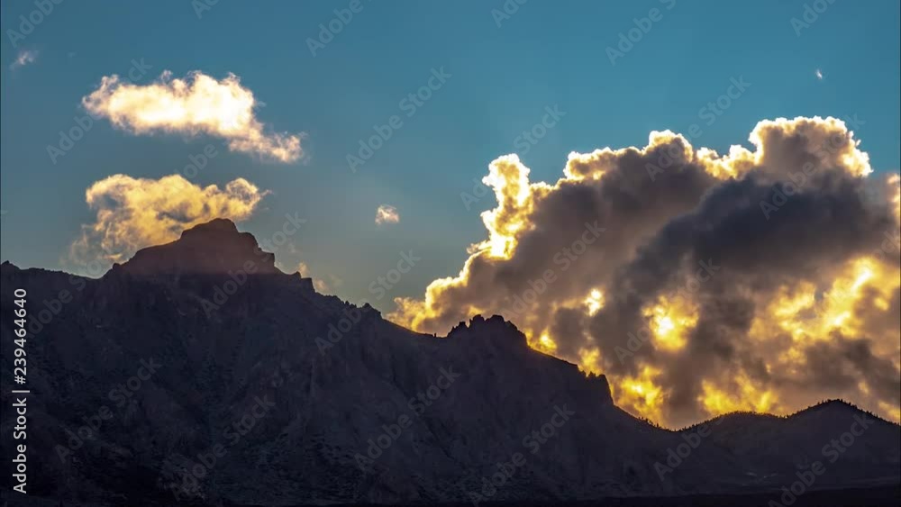 Poster time lapse view as light rays explode through clouds and shine over jagged mountaintops. clouds roll