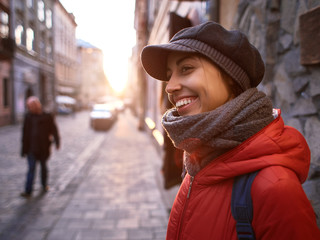 young woman in red jacket and gray cap walking on the street at evening