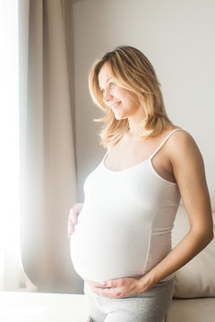 Pregnant woman is standing near the window