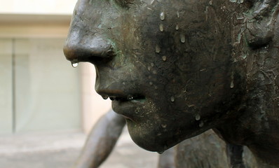 Detalle de cara de escultura metálica con gotas de lluvia cayendo