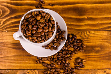 White cup filled with coffee beans on wooden table. Top view