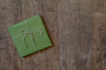 Present box warpped in green kraft paper on wooden background. Flat lay style, top view, copy space.
