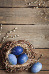 Easter background. blue eggs in a nest of straw and willow branches on a wooden table.