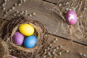 Easter background. colorful eggs in a nest of straw and willow branches on a wooden table. drawing on a stencil in the form of an Easter bunny