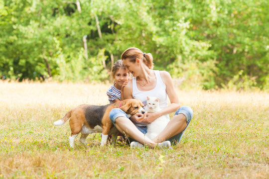 Adorable couple daughter and mom sitting on a grass with their pets