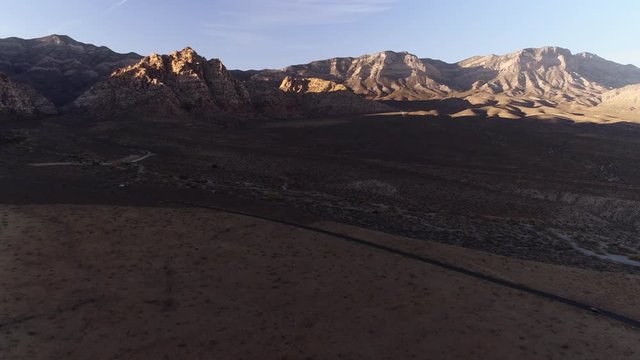 A drone shot opening on a curved road in a vast valley with spectacular mountains on a horizon
