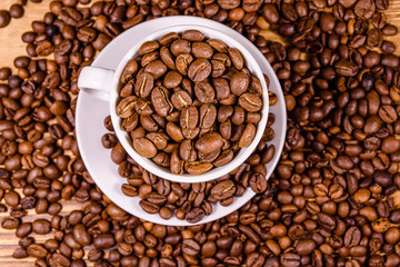 White cup filled with coffee beans on wooden table. Top view