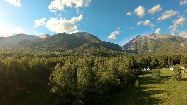 Aerial shot above the meadow and trees. Flight to the mountains. Drone flies forward over the green field and forest, flying beside a Buddhist temple