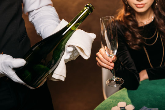 cropped image of waiter pouring champagne in glass for girl at poker table in casino