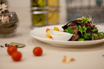 Meat, fish, salads on the table in white plate in the interior with olive oil