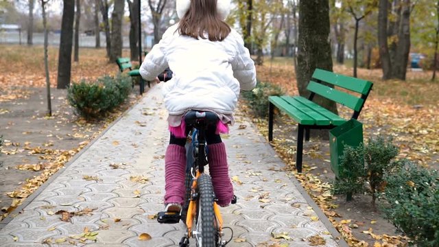 One caucasian children rides bike road in autumn park. Little girl riding black orange cycle in park. Kid goes do bicycle sports.