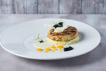 Fish cutlets garnished with potato puree on a white plate yellow deops from sauce. prepared by chef