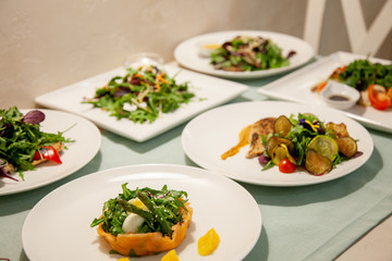 Meat, fish, salads on the table in white plate in the interior with olive oil