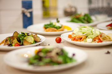 Meat, fish, salads on the table in white plate in the interior with olive oil