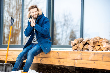 Portrait of a handsome man in winter clothes filling cold sitting on the terrace of the modern house