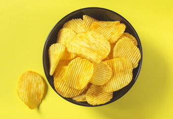 Potato chips in black bowl on yellow background, top view