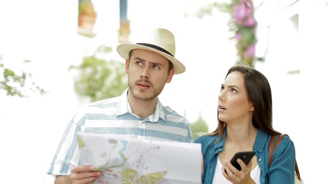 Confused tourists searching location comparing phone and map on vacation