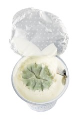 An open pot of yogurt that has gone off with green mold on a white background