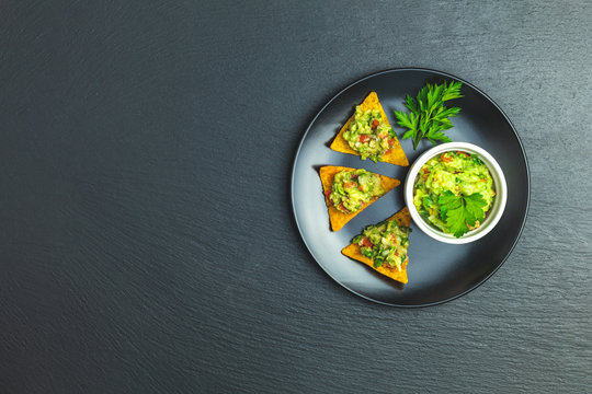 Guacamole and nachos with ingredients on the background of a black stone board