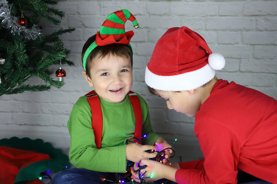 niños felices agarrando guirnalda de luces en navidad disfrazados de duende y Santa Claus 
