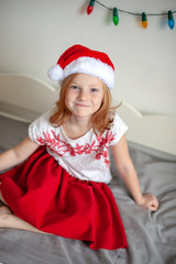 Girl in santa claus hat sitting on the bed