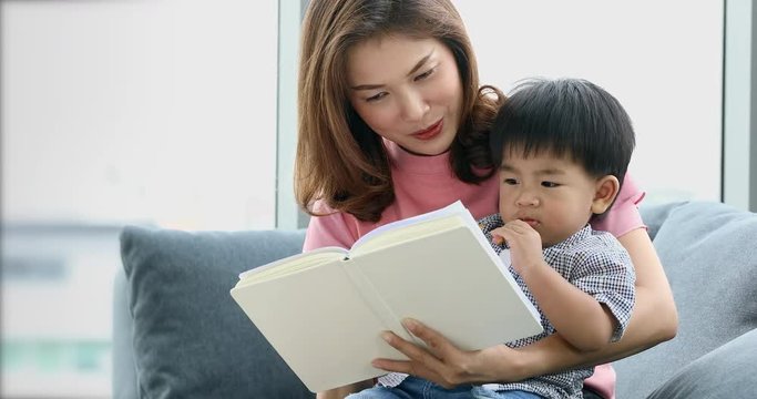 Asian mother and her son sitting on sofa together, their reading some book, sharing their happy time, concept for mother and son.