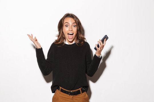 Image of emotional woman 20s screaming and holding smartphone while standing, isolated over beige background