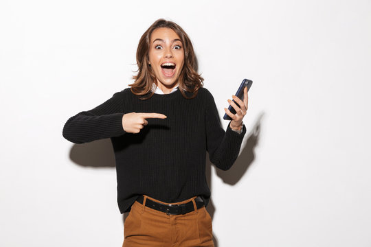 Image of pretty woman 20s screaming and holding mobile phone while standing, isolated over beige background