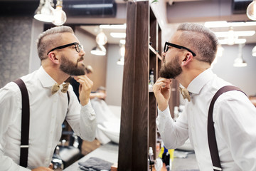 Hipster man client with glasses looking in the mirror in barber shop.