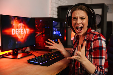 Angry girl gamer sitting at the table, playing online games © Drobot Dean