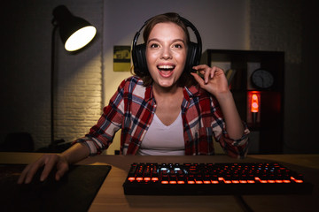 Excited girl gamer sitting at the table, playing online games