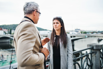 Man and woman business partners walking by a river in city of Prague, talking.