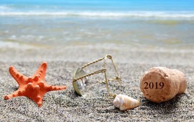 Cork stopper of champagne with number 2019 and seashell with starfish on sand beach. Happy New Year...