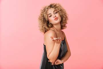 Fototapeta premium Portrait of gorgeous curly woman 20s wearing dress smiling while standing, isolated over pink background