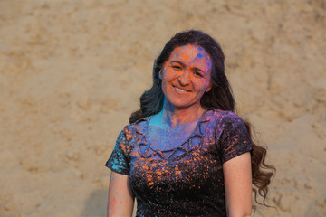 Positive brunette woman with long curly hair covered with colorful dry powder Holi at the desert. Empty space